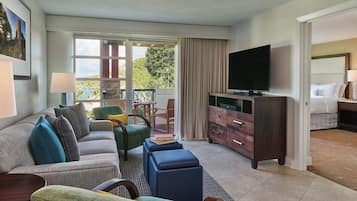 A hotel room with a sofa, chairs, a TV, a bed, and a balcony with a view.