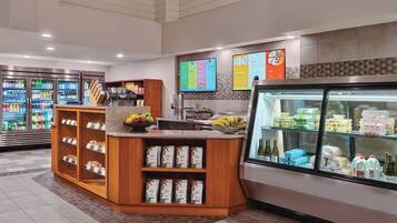 A self-service beverage station with refrigerated drinks, a fruit bowl, and packaged food items.