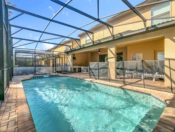 An indoor swimming pool with a clear view of the pool area, surrounded by a covered patio with seating and a glass enclosure. - Spacious 8BR Luxury Home, Pool,Spa, By Disney (Kissimmee)