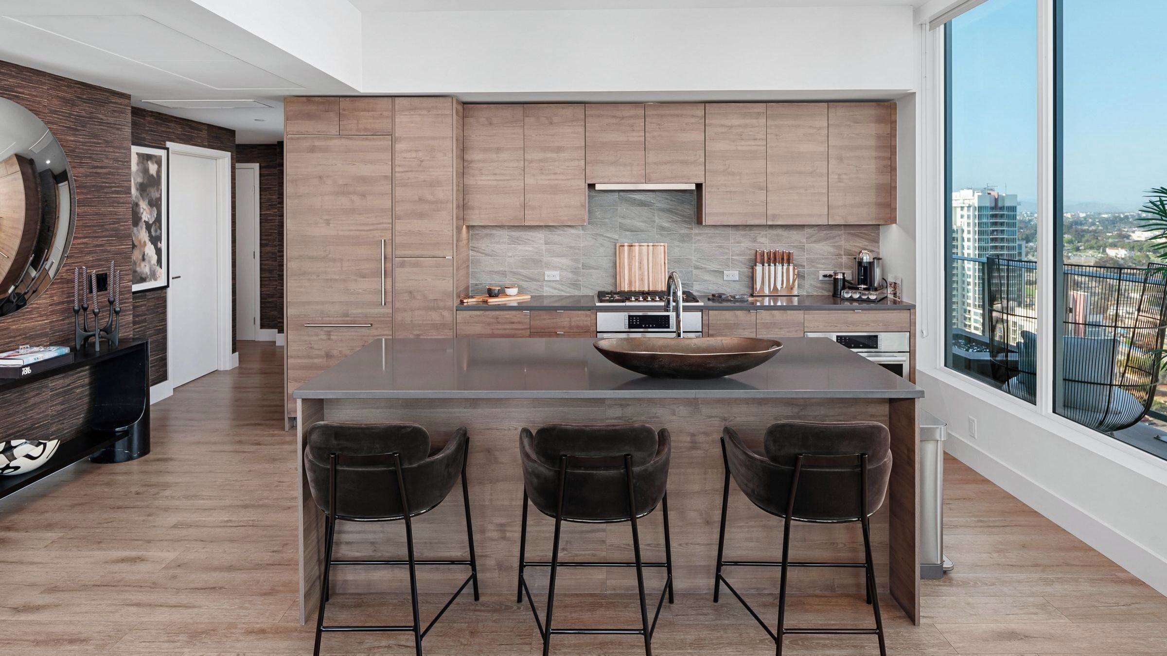 Una cocina moderna con una isla central, taburetes de bar y un amplio ventanal con vistas a la ciudad.
