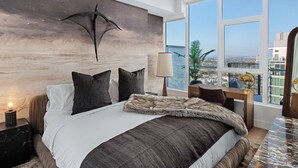 A modern bedroom with a large bed, a desk, a lamp, and a view of the city. - 41st Floor! 2bdr w/ Luxury Amenities & Balcony Skylux Penthouse by Avantstay (San Diego)