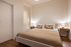Ein ordentlich eingerichtetes Schlafzimmer mit einem großen Bett, zwei Nachttischen mit Lampen und einer Tür.