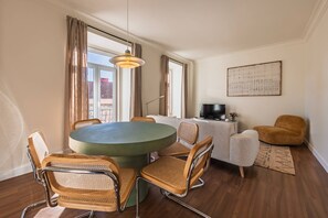 Ein modernes Wohnzimmer mit einem runden Tisch, Korbstühlen, einer Couch und einem Fernseher.