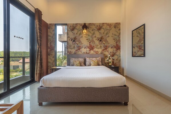 A bedroom with a large bed, a nightstand, a wall-mounted light, and a window with curtains. - RETRO VILLA  (Lonavala)