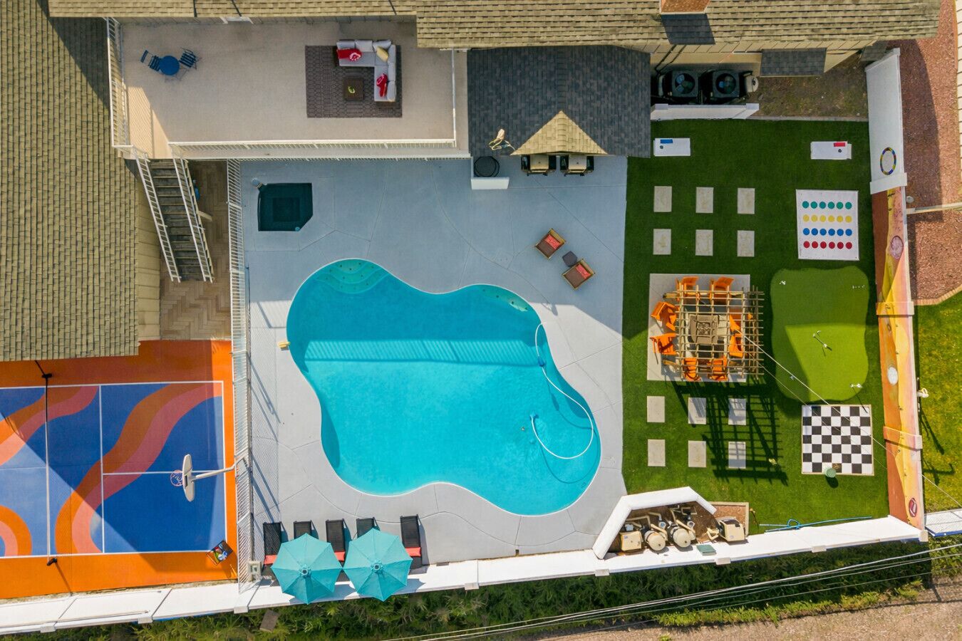 Vue aérienne d’une propriété résidentielle dotée d’une piscine, d’une terrasse avec mobilier d’extérieur et d’un petit jardin aménagé avec un motif à carreaux.