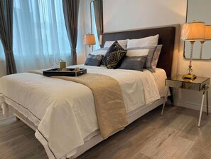 Ein ordentlich bezogenes Bett mit einer Nachstischplatte und Gläsern, einer Nachttischlampe und einem Nachttisch.
