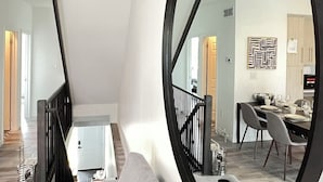 Een moderne woonkamer met een grote ronde spiegel, een trap en een eethoek met een tafel en stoelen.