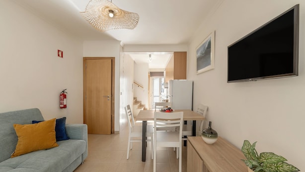 Una sala de estar moderna con un sofá, una mesa de comedor y sillas. Hay un televisor de pantalla plana en la pared, un extintor y una planta en maceta.
