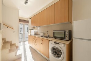 Eine Küche mit Holzschränken, einer Mikrowelle, einer Waschmaschine und einem Kühlschrank.