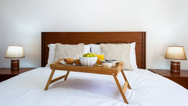 Cama bem arrumada com uma bandeja de itens de café da manhã, incluindo uma tigela de frutas, um muffin e um copo de suco de laranja.