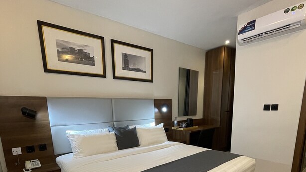 A hotel room with a large bed, a bedside table with a phone, a mirror, and framed pictures on the wall. - Ringruby Hotel Value County (Lekki)