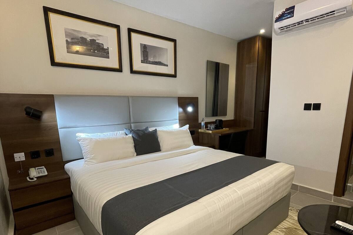 A hotel room with a large bed, a bedside table with a phone, a mirror, and framed pictures on the wall.