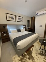 A hotel room with a large bed, a bedside table with a phone, a mirror, and framed pictures on the wall.