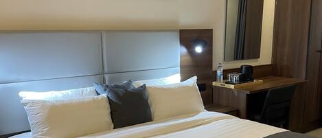 A neatly made bed with white and gray linens, a wooden headboard, and a bedside table with a water bottle and a cup.