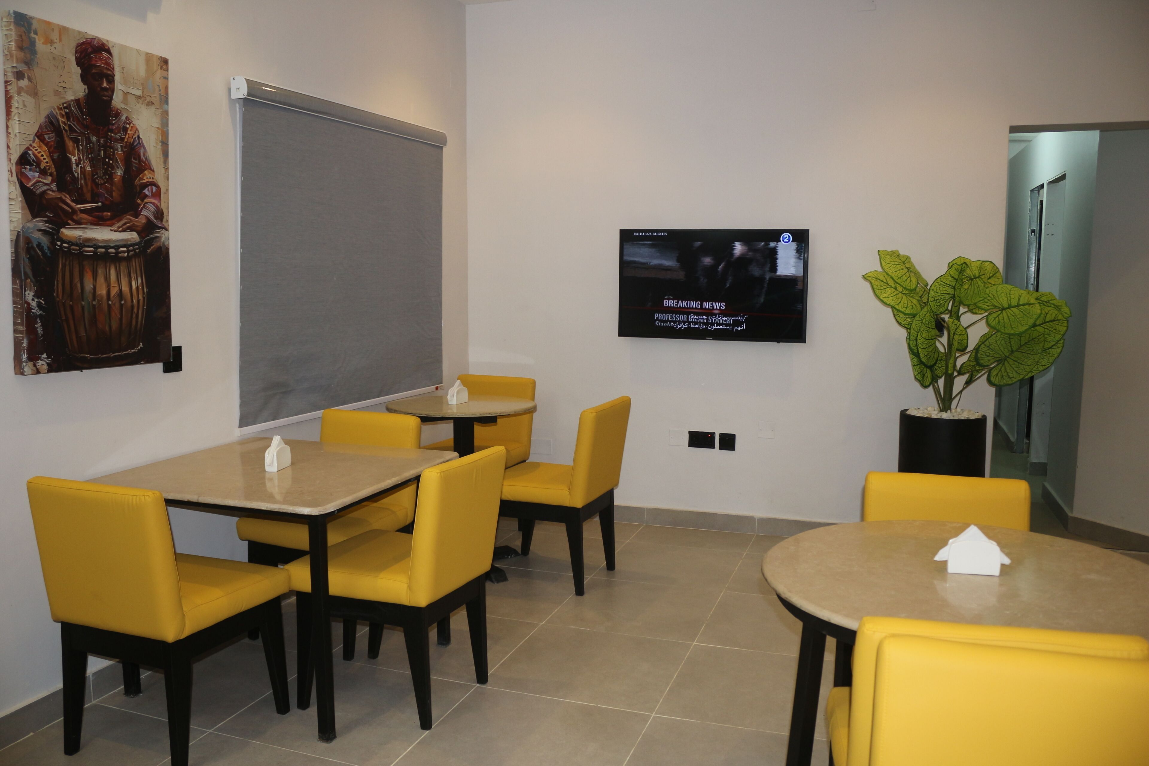A conference room with yellow chairs and tables, a large screen, and a poster on the wall.