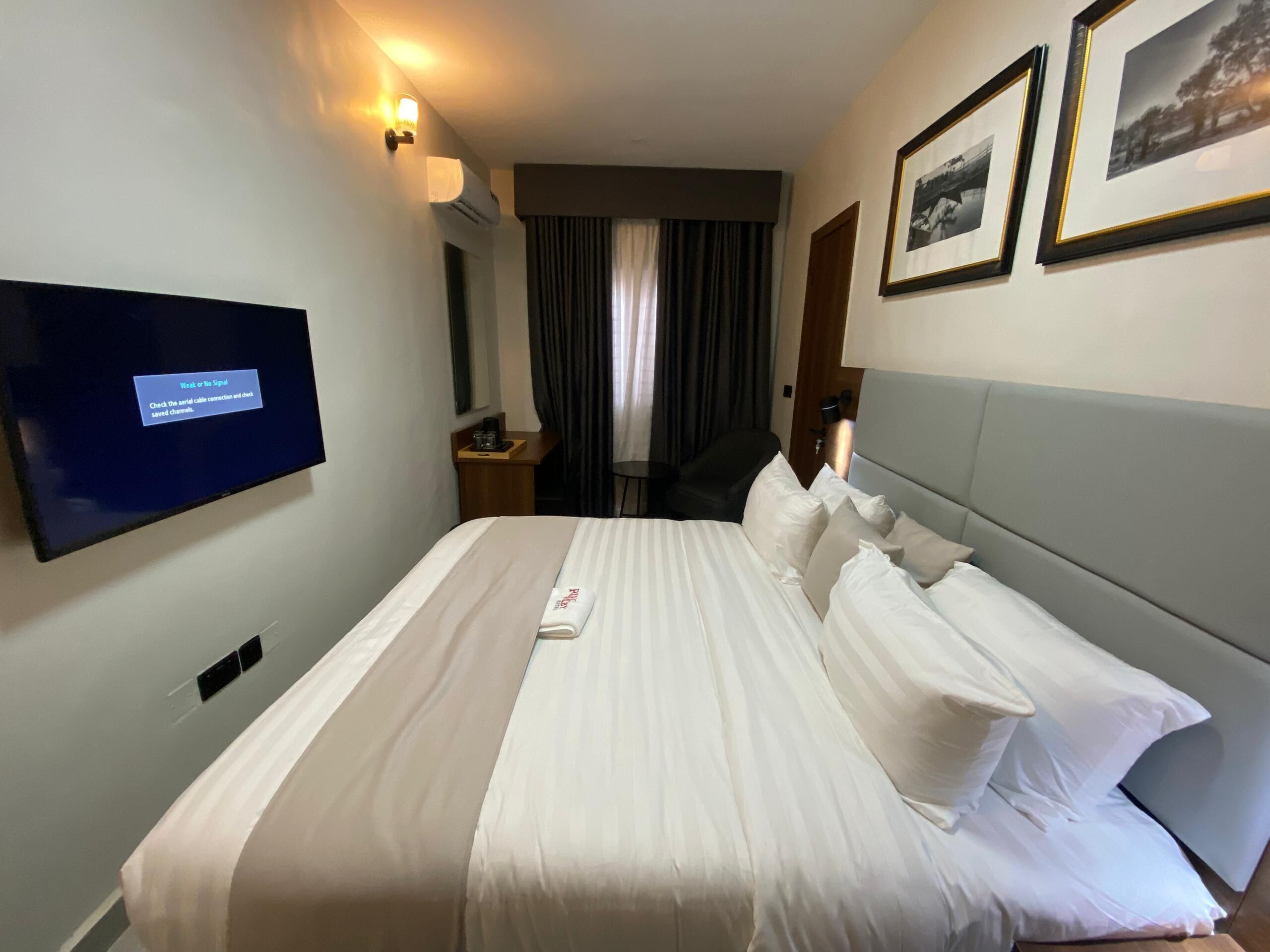 Ein Hotelzimmer mit Bett, Wand-Fernseher, Schreibtisch mit Stuhl und einem Vorhangfenster.