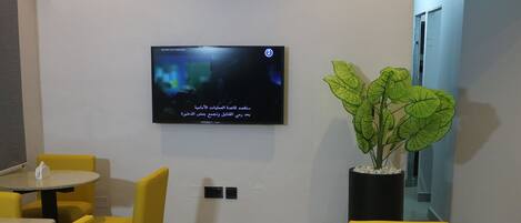 A conference room with yellow chairs, a round table, a flat-screen TV on the wall, and a potted plant.