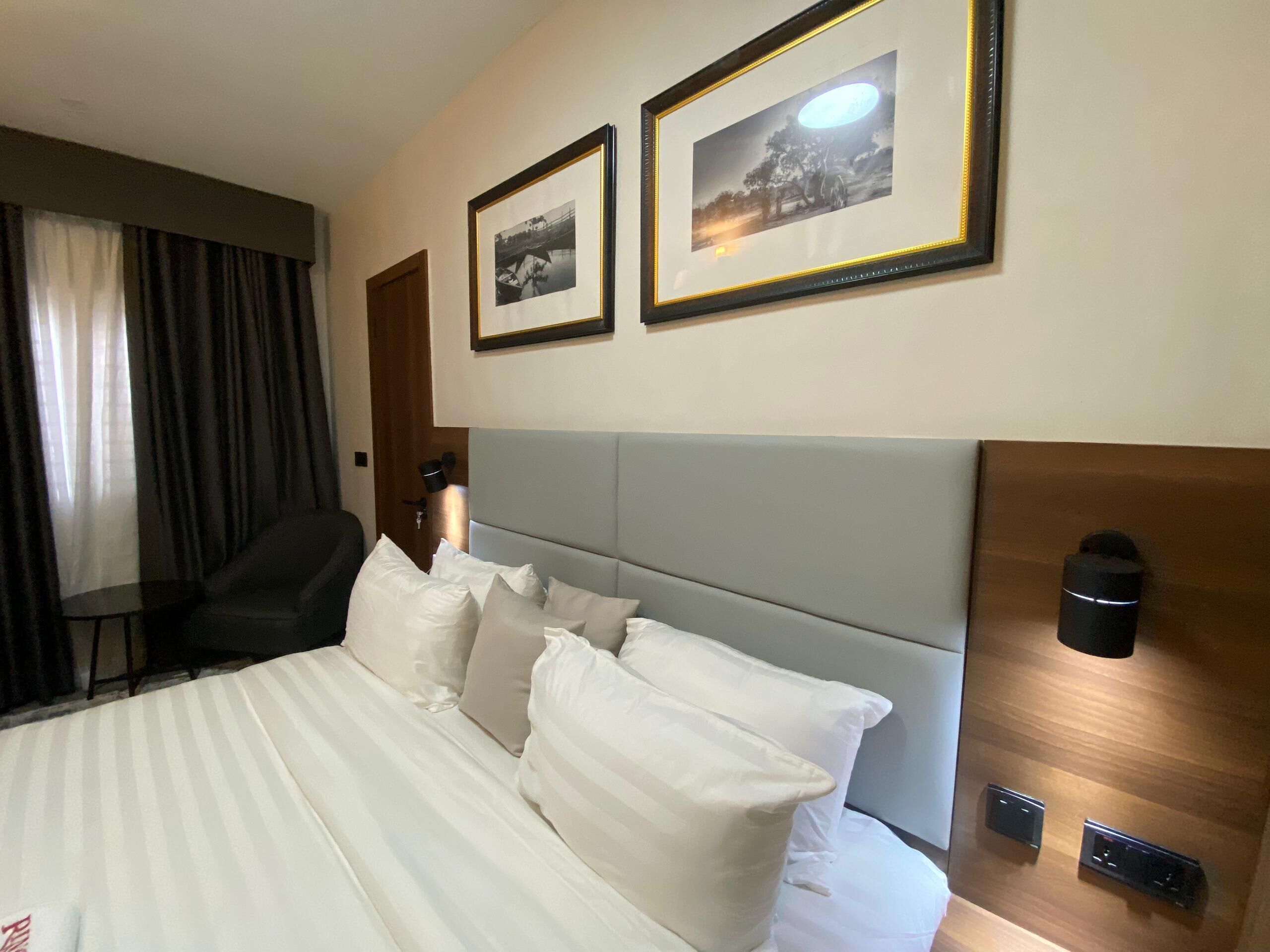 A hotel room with a large bed, a headboard, two framed pictures on the wall, a desk, and a chair.