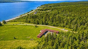 Ilmakuva kiinteistöstä, jossa on suuri vesialue, tiheä metsä ja huomiota herättävä punainen rakennus.