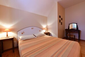 Una cama bien hecha con una colcha a rayas, dos lámparas de noche, una mesita de noche de madera y un aparador con espejo.