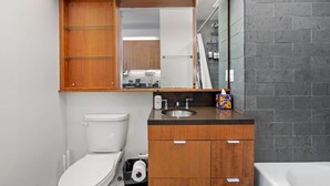 A modern bathroom with a wooden vanity, a sink, a toilet, and a large mirror. - Studio apt walkable to Oracle Park (San Francisco)