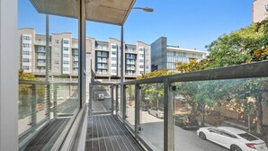 A glass-walled corridor with a metal grate floor, leading to a parking area with cars and a building in the background. - Studio apt walkable to Oracle Park (San Francisco)
