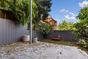 A backyard with a grey fence, a wooden deck, a red bench, and two cylindrical planters. - Modern 1BR Noe Valley Apt with laundry & backyard (San Francisco)