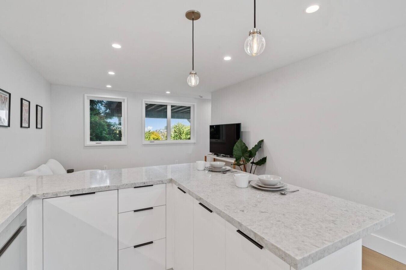 A modern kitchen with white cabinetry, a marble countertop, pendant lighting, and a large window.