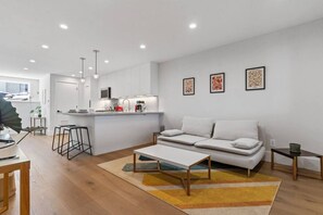 A modern living room with a sofa, coffee table, and a kitchen area with a sink and stove.