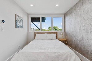 A bedroom with a bed, a window with a view, a nightstand, and a wall with a textured pattern. - Modern 1BR Noe Valley Apt with laundry & backyard (San Francisco)