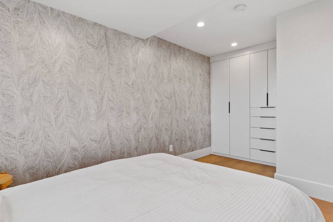Een slaapkamer met een bed, een kledingkast en een wand met een structuur.