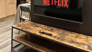 Moderni keittiö, jossa on ruokapöytä ja -tuolit. Seinälle on asennettu televisio, jossa näkyy Netflixin logo, ja television yläpuolella on kehystetty taideteos.