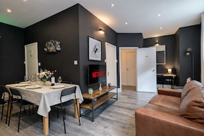Ein modernes Wohnzimmer mit einem braunen Ledersofa, einem Essbereich mit einem weißen Tisch und einem an der Wand befestigten Flachbildfernseher.