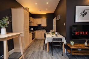 A compact kitchen with wooden cabinets, a dining table set for two, and a television displaying the Netflix logo. - Classy 2 bedroom Flat in SHoreditch's Heart (London)