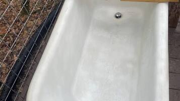 A white outdoor bathtub with a wooden tray on top, surrounded by a metal fence.