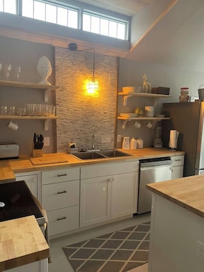 Een moderne keuken met een achterwand van steen, houten aanrechtbladen en witte kasten.