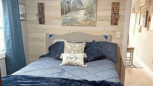 Un lit avec une tête de lit, un tableau au mur et une fenêtre avec des rideaux.