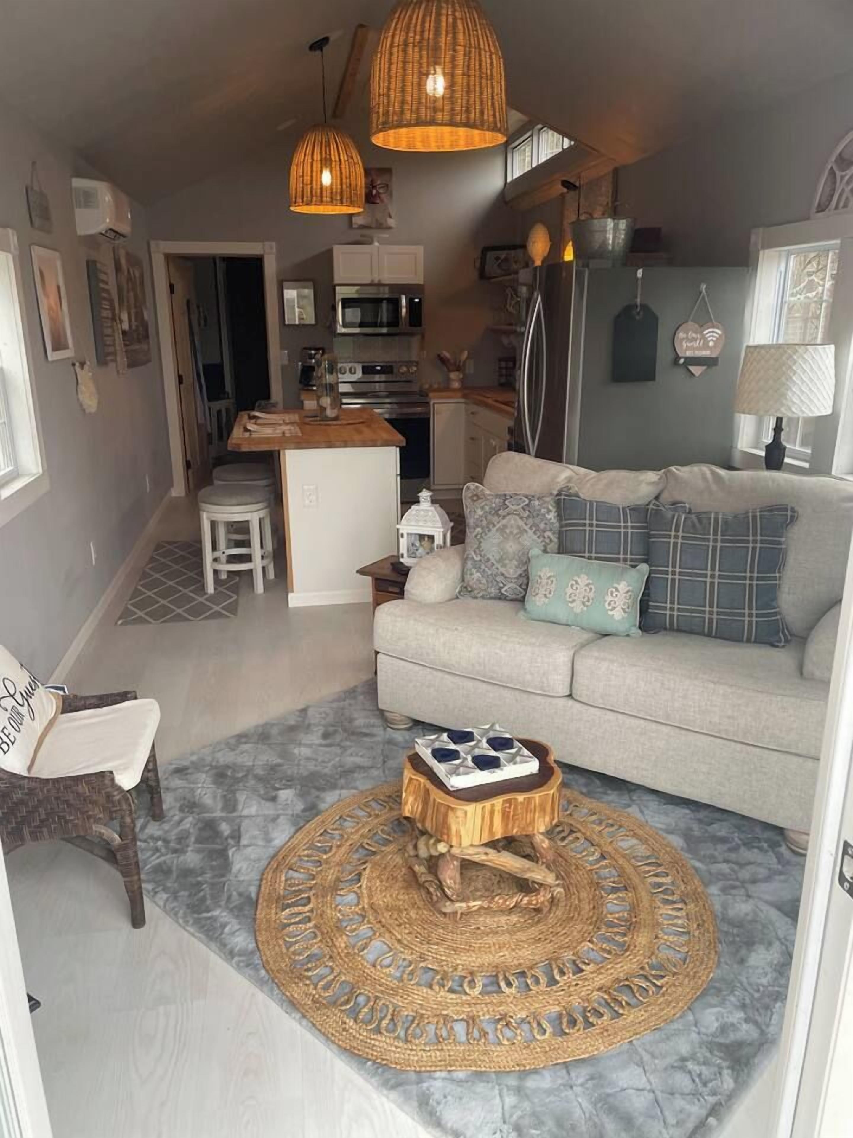A compact living space with a kitchenette, a sofa with patterned cushions, a wicker coffee table, and a woven rug.