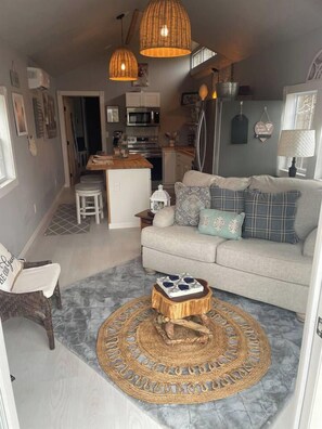 A compact living space with a sofa, a coffee table, a wicker chair, and a kitchen area with a microwave and refrigerator. - Sleepy Valley Cabin | Hot Tub & Scenic Views (Madisonville)