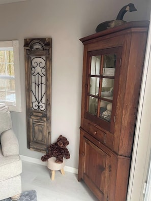 Een kamer met een houten kast, een decoratief wandobject en een klein krukje met een knuffeldier.
