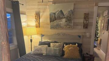 A bedroom with a bed, a ceiling fan, a painting, and a nightstand.
