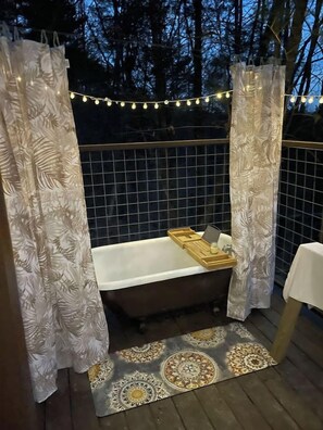 Une terrasse en bois avec une baignoire, un tapis à motifs et des guirlandes lumineuses.