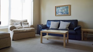En stue med en beige sofa, en mørkeblå sofa, et træsofabord og et billede på væggen.