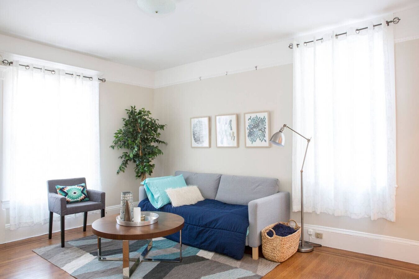 A living room with a grey sofa, a round coffee table, a side table, a chair, a plant, and a floor lamp.