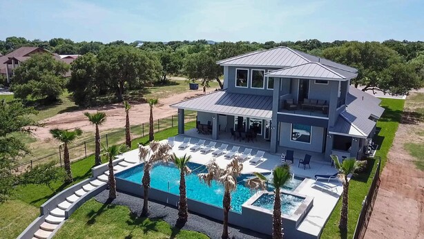 A two-story house with a large pool, surrounded by palm trees and a fenced yard. - Lazy Haven Resort: Luxury Lakefront Estate on Lake LBJ with Private Pool Hot Tub (Kingsland)