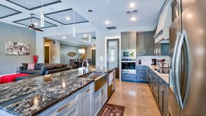 A modern kitchen with a marble island, stainless steel appliances, and a dining area with a sofa and chairs. - Lazy Haven Resort: Luxury Lakefront Estate on Lake LBJ with Private Pool Hot Tub (Kingsland)