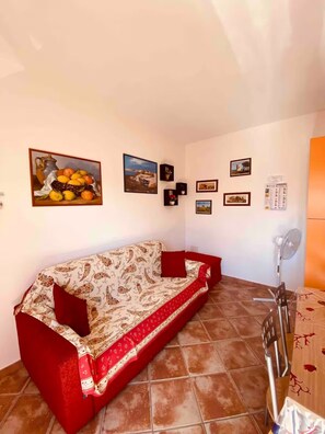 Un salon avec un canapé, un ventilateur et divers tableaux encadrés accrochés au mur.