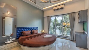 Ein modernes Schlafzimmer mit einem runden Bett, einem Deckenventilator und einem großen Fenster mit Blick auf Palmen.