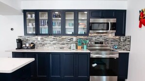 A modern kitchen with dark cabinets, a stainless steel oven, a microwave, and a coffee machine. - Ultimate Beach Getaway (Fort Myers Beach)