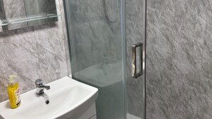 Une salle de bain moderne avec une douche à parois de verre, un lavabo blanc doté d’un distributeur de savon et des murs en marbre.
